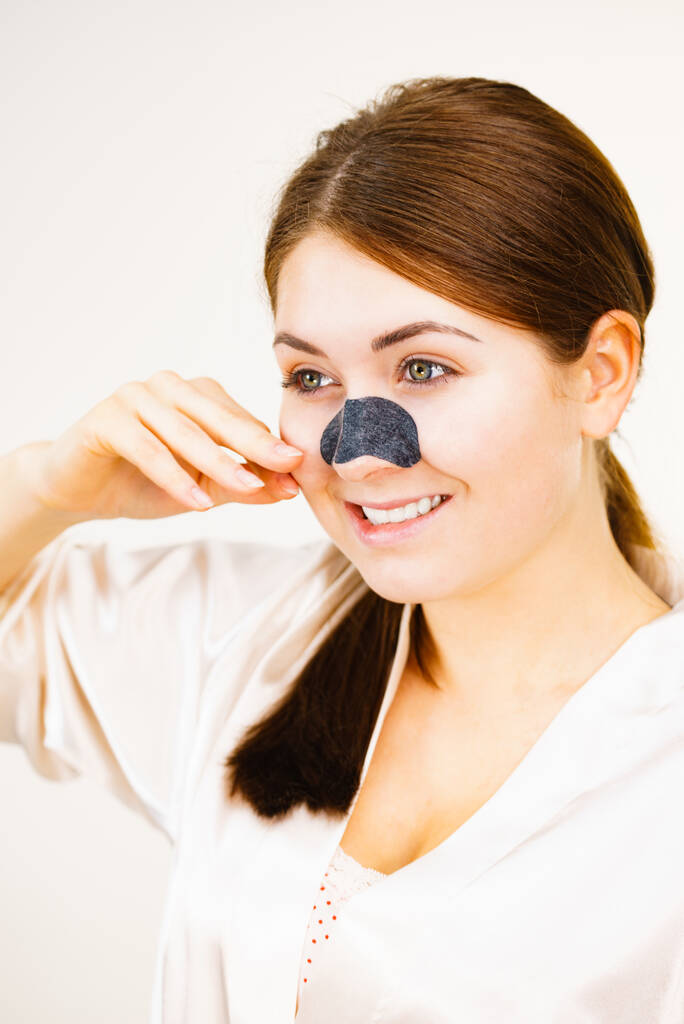 Femme appliquant des bandes claires sur le nez, à l'aide d'un masque textile nettoyant les pores, sur blanc. Fille prenant soin du teint de la peau. Soins de beauté. Soins de la peau. - Photo, image