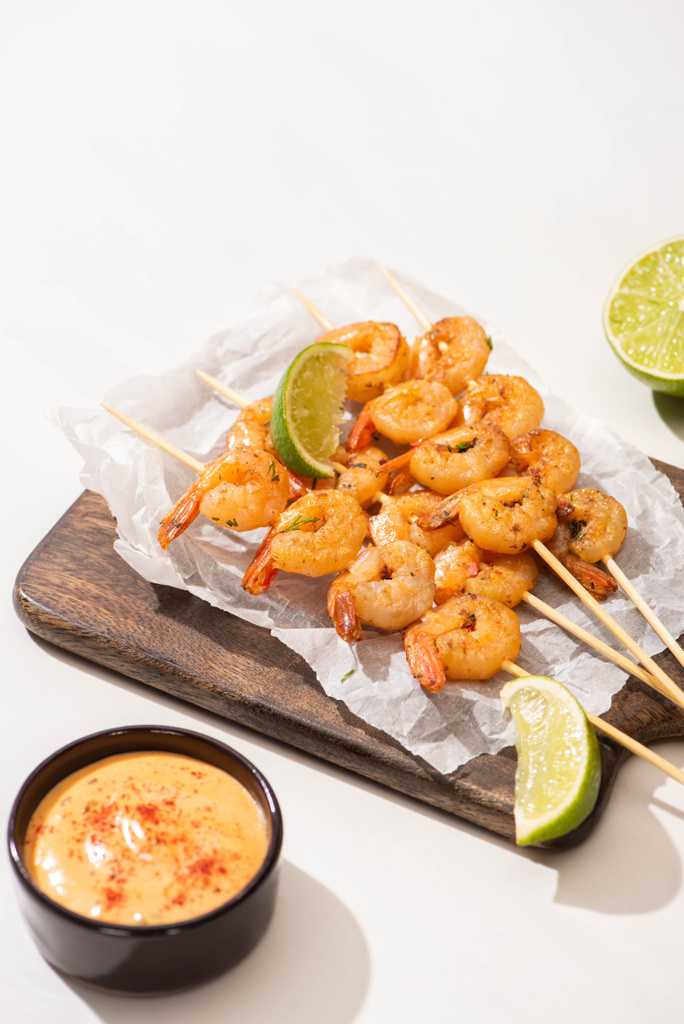 prawns on skewers with lime and sauce on parchment paper on wooden board on white background - Photo, Image