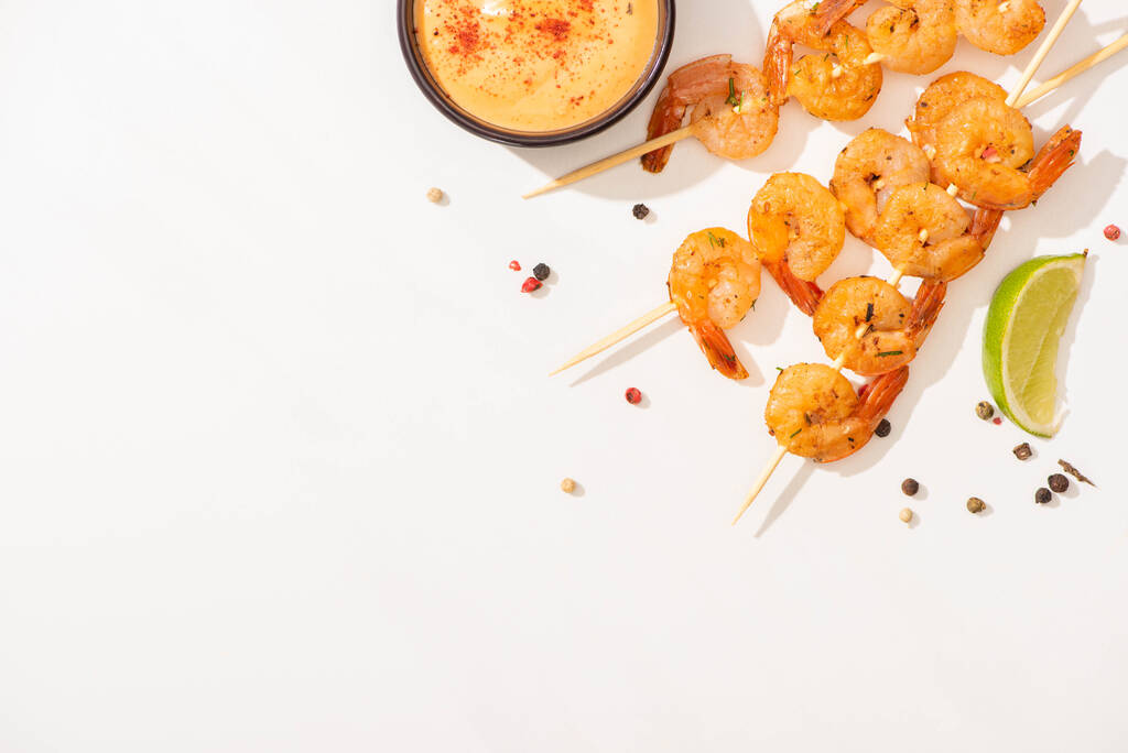 vista superior de deliciosos camarões fritos em espetos com molho, limão e pimenta no fundo branco
 - Foto, Imagem