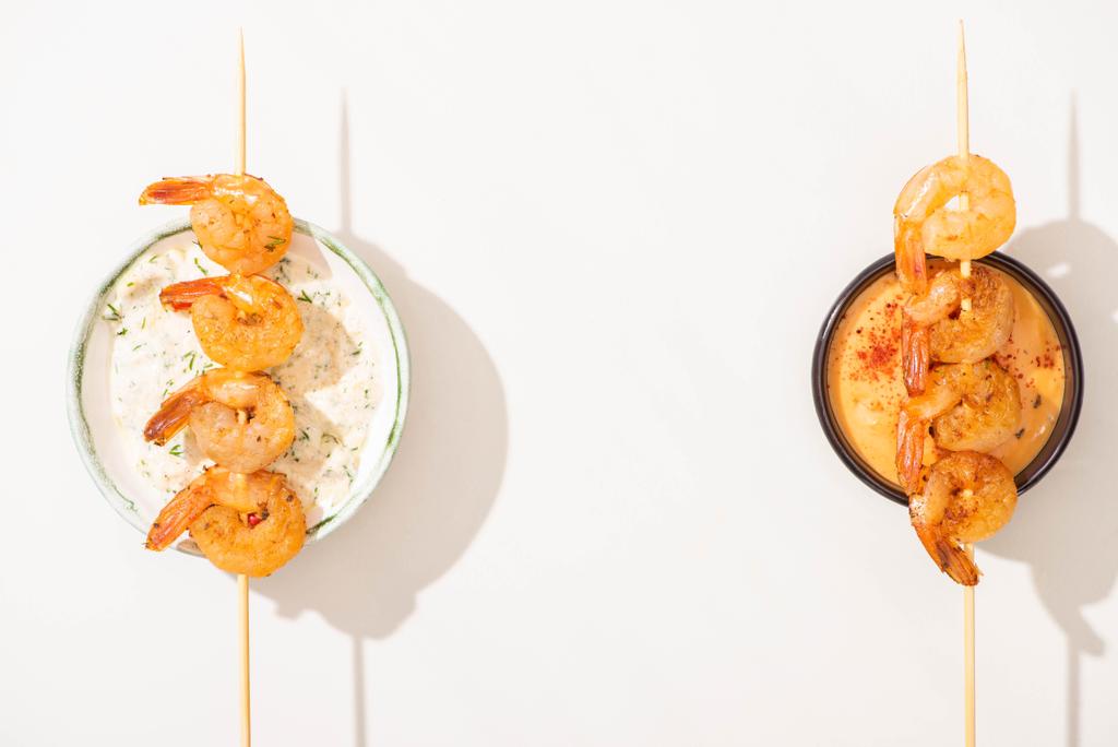 vista superior de deliciosos langostinos fritos en pinchos con salsas sobre fondo blanco
 - Foto, imagen