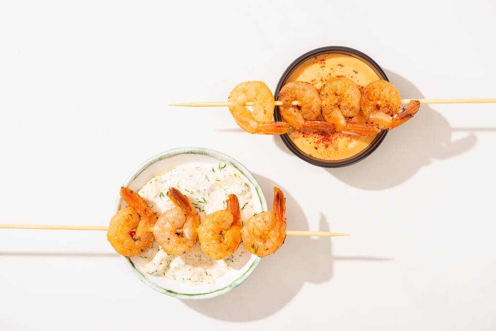 vista superior de deliciosos camarões fritos em espetos com molhos no fundo branco
 - Foto, Imagem
