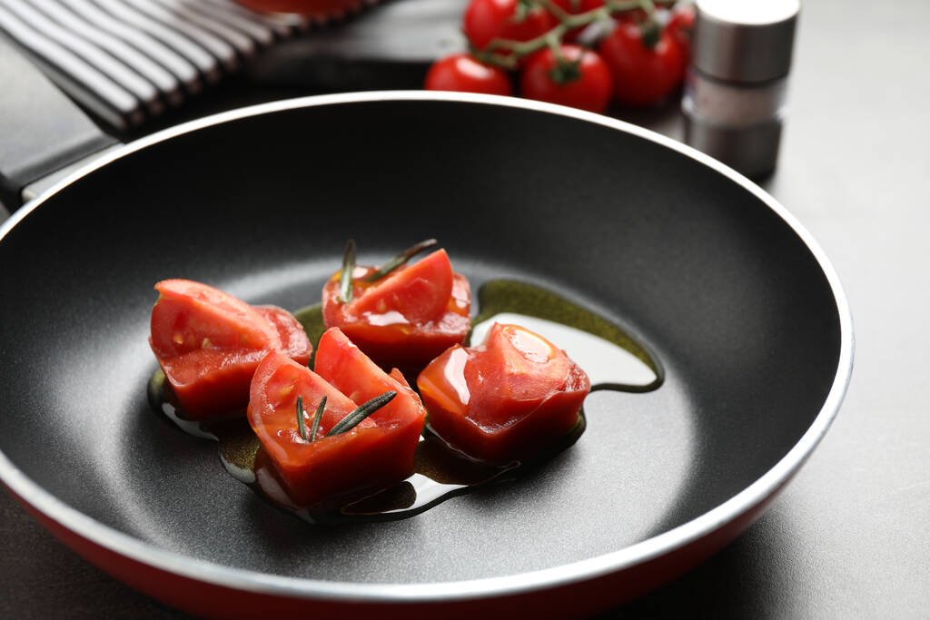 Cubos de gelo derretendo com tomate, óleo e alecrim na mesa cinza
 - Foto, Imagem