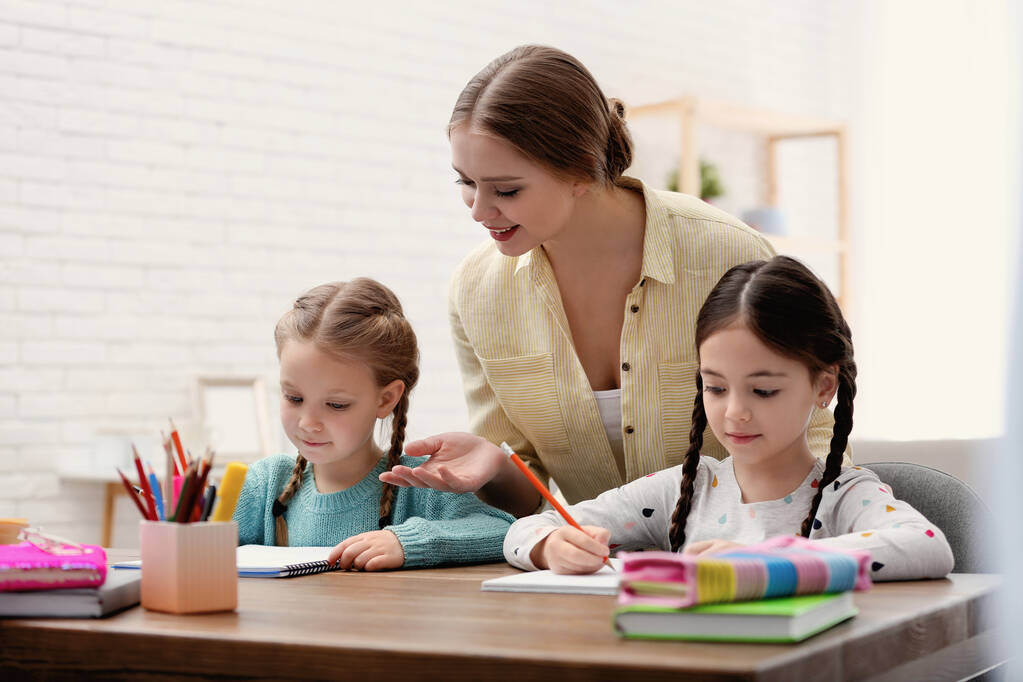 Mother helping her daughters with homework at table indoors - Photo, Image