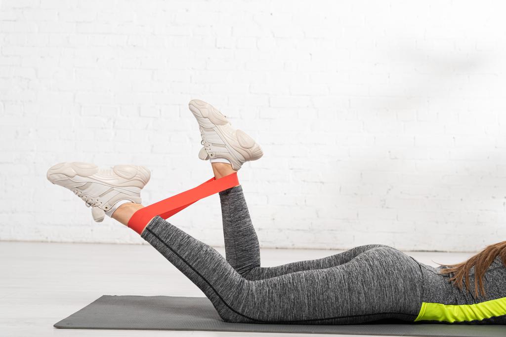 обрезанный вид спортивной женщины, лежащей на фитнес-коврик и разработка с сопротивлением полосы
 - Фото, изображение