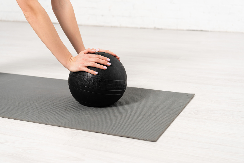 vista cortada de menina tocando bola preta no tapete de fitness
  - Foto, Imagem