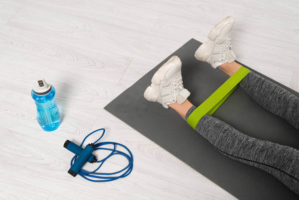 cropped view of woman working out with resistance band near skipping rope and sports bottle  - Photo, Image