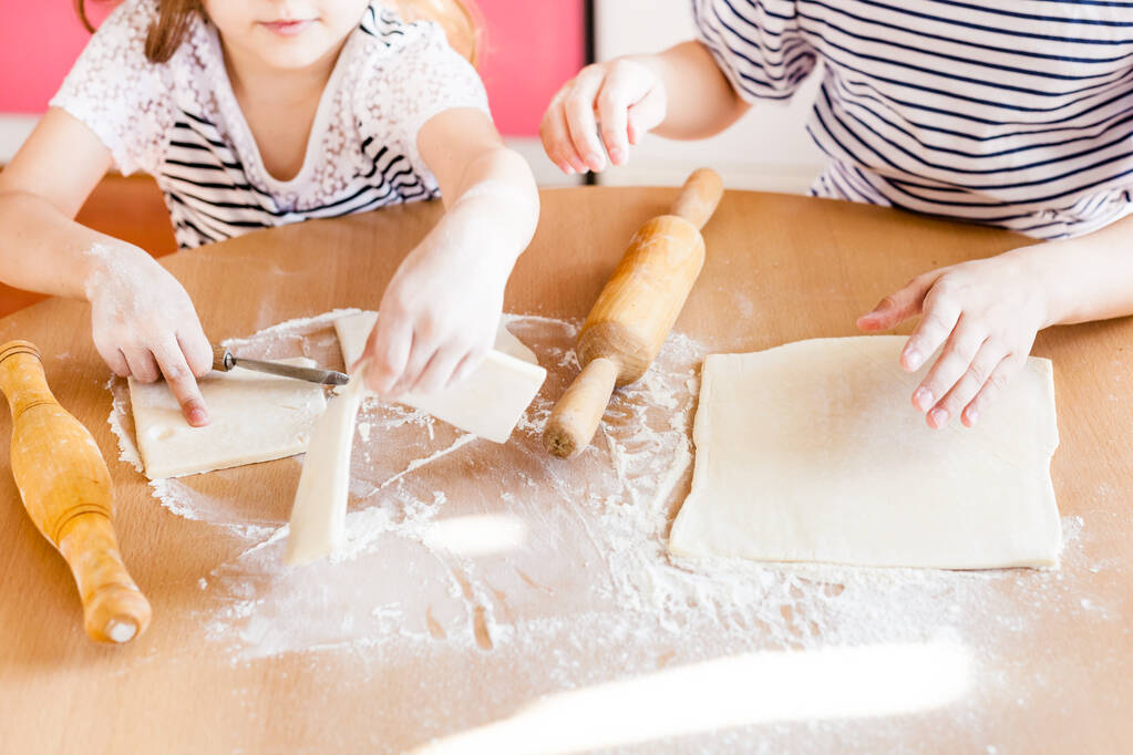 Ein Mädchen und eine kleine Schwester kochen in der Küche am Tisch Gebäck, Mehl und Nudelholz, Kochen mit Kindern, leckeres Essen, Junk Food, Kohlenhydrate, Frühstück, Croissants - Foto, Bild