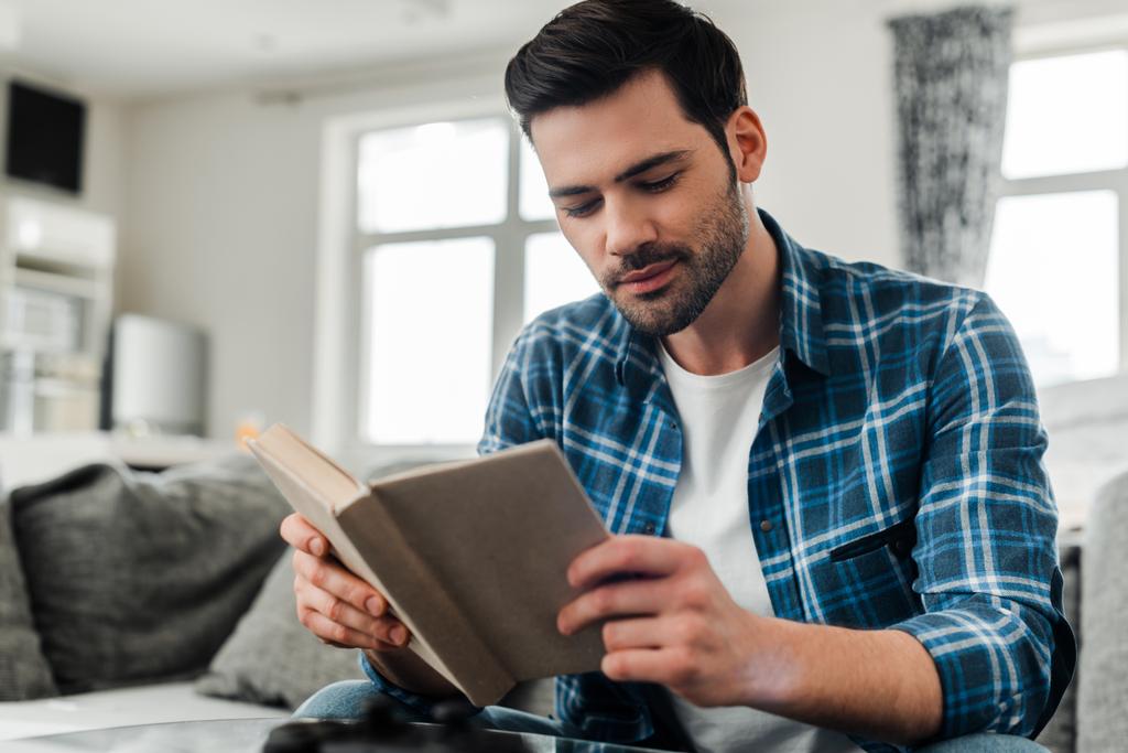 Вибірковий фокус красивого чоловіка в плетеній сорочці читання книги вдома
 - Фото, зображення
