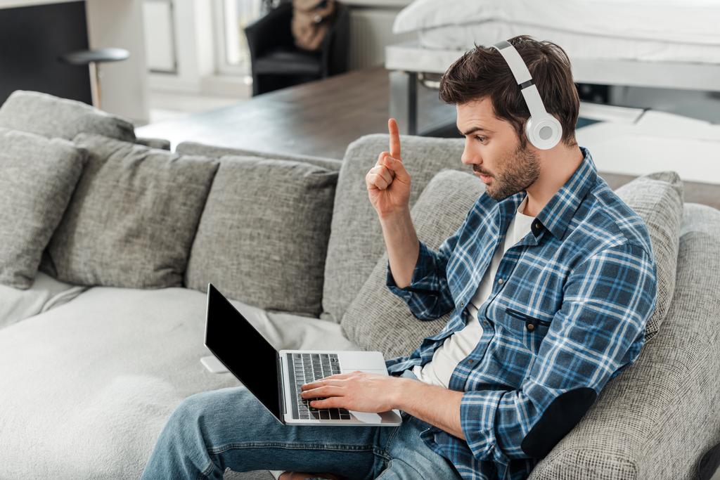 Freelancer em fones de ouvido tendo ideia e usando laptop no sofá em casa
  - Foto, Imagem