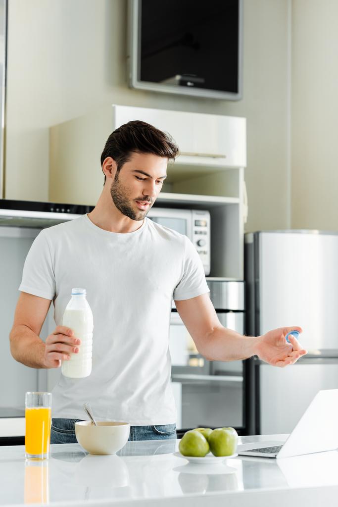 Mutfakta dizüstü bilgisayarla görüntülü sohbet ederken elinde süt şişesi tutan adam.  - Fotoğraf, Görsel