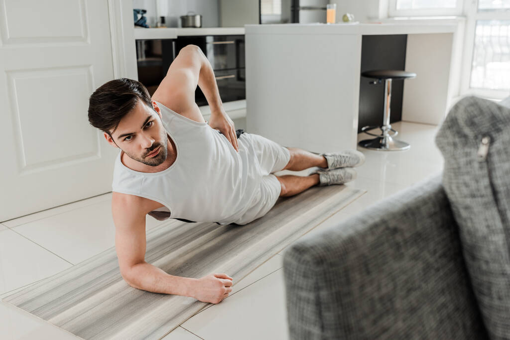 Concentration sélective de l'homme regardant la caméra tout en faisant planche sur tapis de fitness à la maison
  - Photo, image