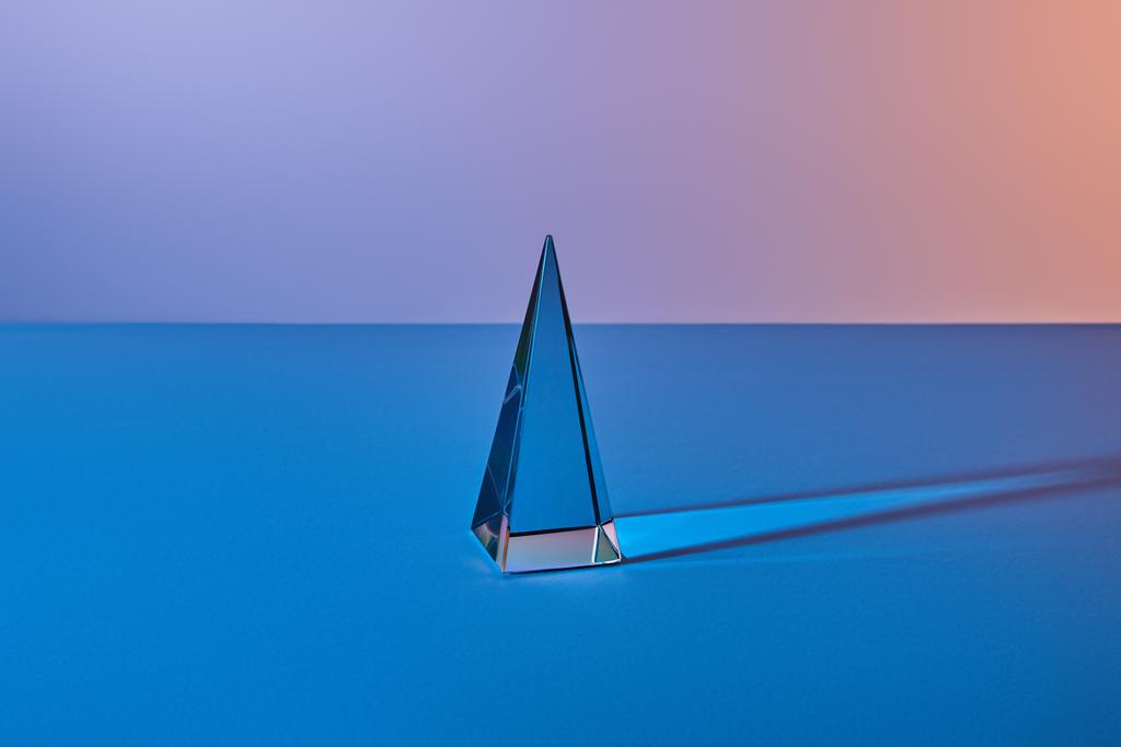 křišťálově průsvitná pyramida se světelným odrazem na modrém pozadí - Fotografie, Obrázek