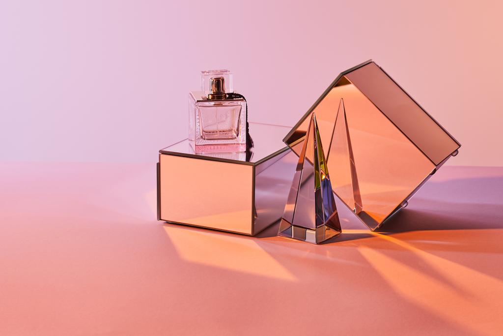 ピンクを背景に香水瓶やミラーキューブの近くに透明なピラミッド - 写真・画像