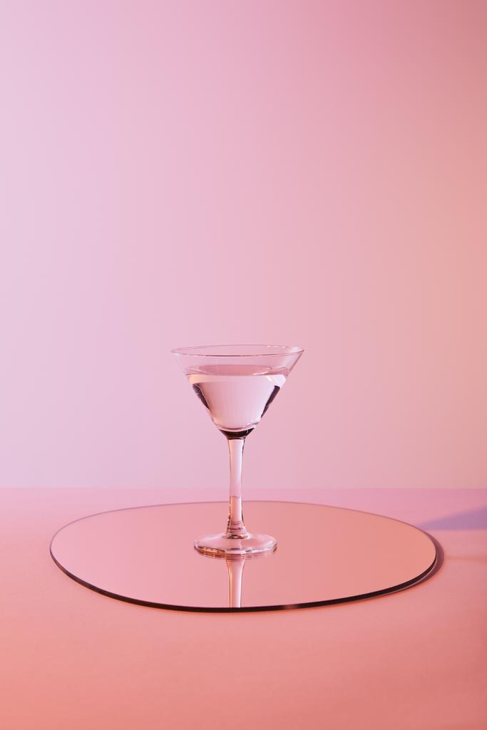 Cocktailglas mit Flüssigkeit auf Spiegel mit Reflexion auf rosa Hintergrund - Foto, Bild