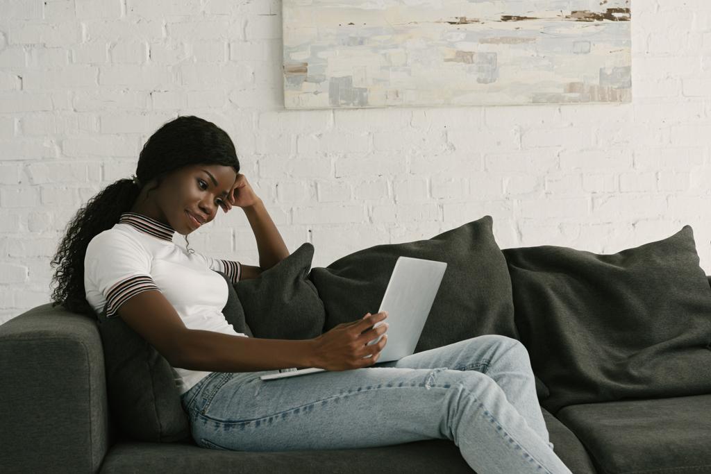 hymyilevä afrikkalainen amerikkalainen freelancer kannettavan tietokoneen kun istuu sohvalla kotona
 - Valokuva, kuva