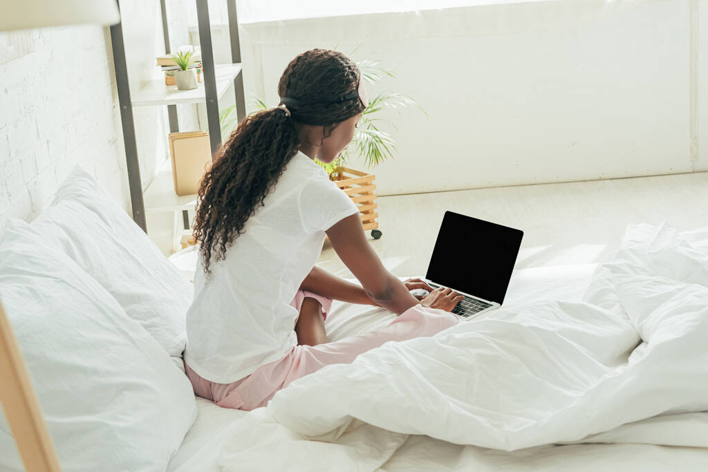 アフリカ系アメリカ人の若いフリーランスがベッドルームに空白の画面でノートパソコンを使い - 写真・画像