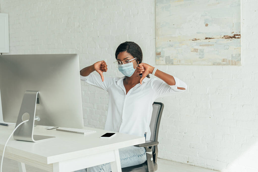 elégedetlen afro-amerikai szabadúszó mutatja hüvelykujját le, miközben ül közelében számítógép monitor otthon - Fotó, kép