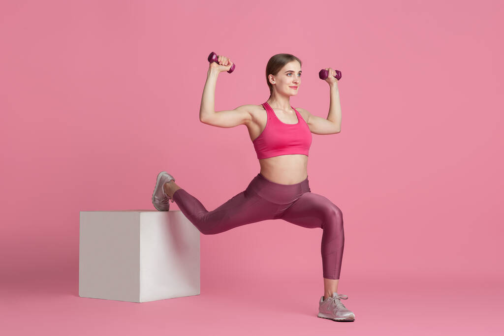 Schöne junge Sportlerin übt auf rosa Studiohintergrund, monochromes Porträt - Foto, Bild