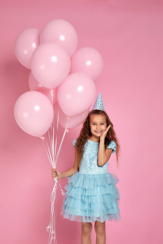 маленькая девочка в платье и шляпе на день рождения празднует с пастельно-розовыми воздушными шарами
 - Фото, изображение