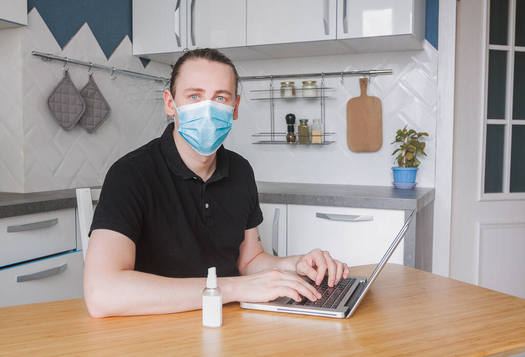 Fiatal férfi szabadúszó orvosi maszkot visel, szabadúszó munkát végez otthonról, e-mailt ír a laptopján. Férfi számítógép segítségével tanulmány online otthon konyha, távolsági internetes munka és önálló karantén - Fotó, kép