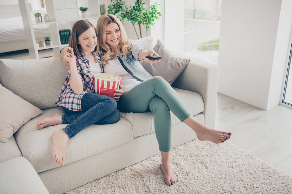 Full body photo of pretty lady mom daughter sit sofa hugging eat popcorn switch on tv set watch favorite comedy stay home quarantine spend time together best friends living room indoors - Photo, Image