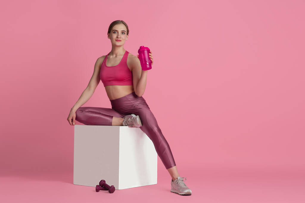 Krásná mladá žena sportovec cvičení na růžové pozadí studia, monochromatický portrét - Fotografie, Obrázek