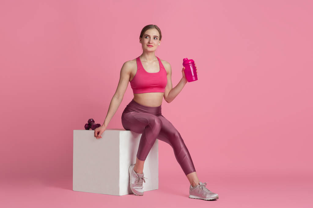 Όμορφη νεαρή αθλήτρια προπονείται σε ροζ φόντο στούντιο, μονόχρωμο πορτρέτο - Φωτογραφία, εικόνα