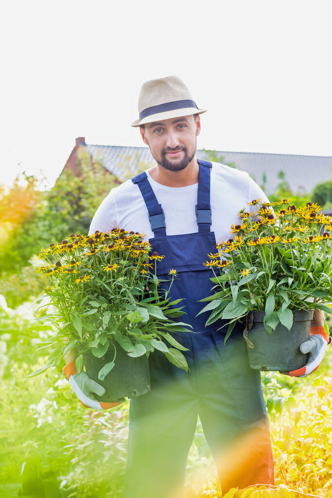 Portrait of mature gardener carrying flowers in shop - Photo, Image