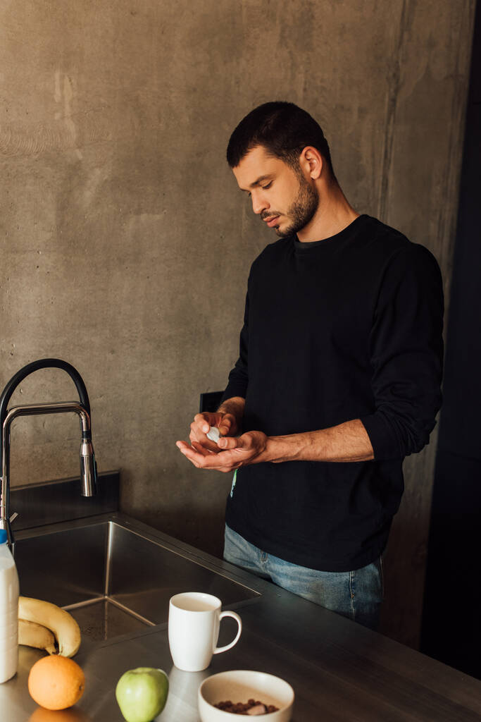 homem barbudo segurando garrafa com higienizador de mão na cozinha
  - Foto, Imagem
