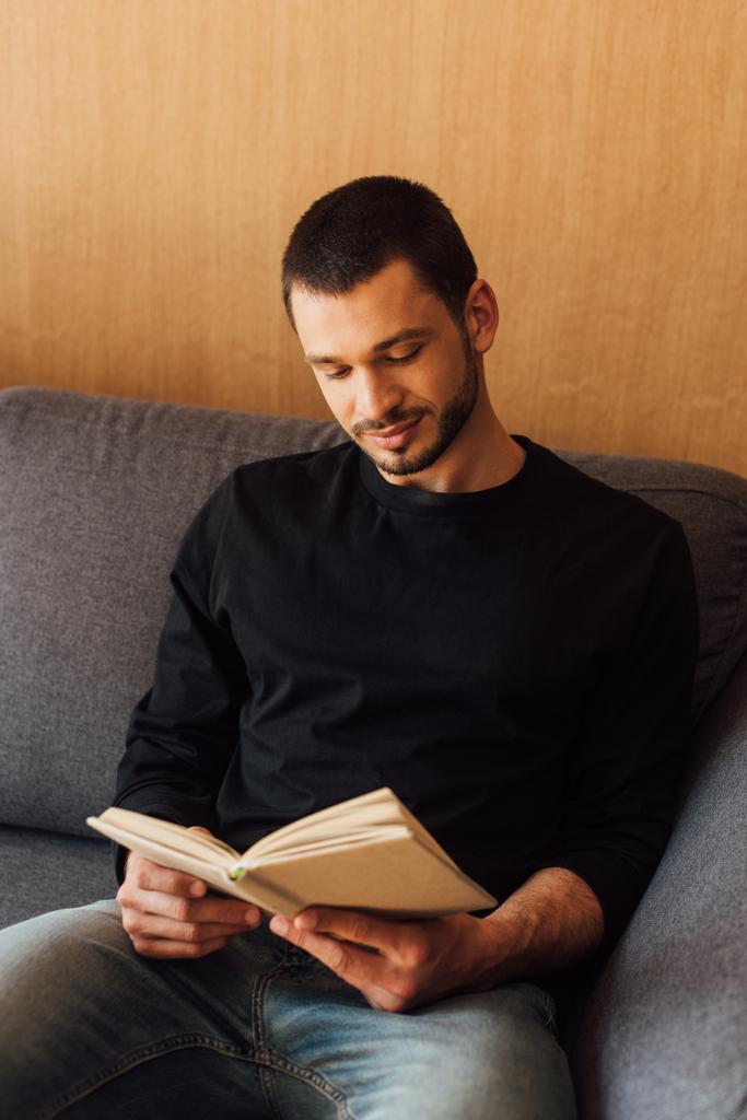 красивий і бородатий чоловік читає книгу, сидячи у вітальні
  - Фото, зображення