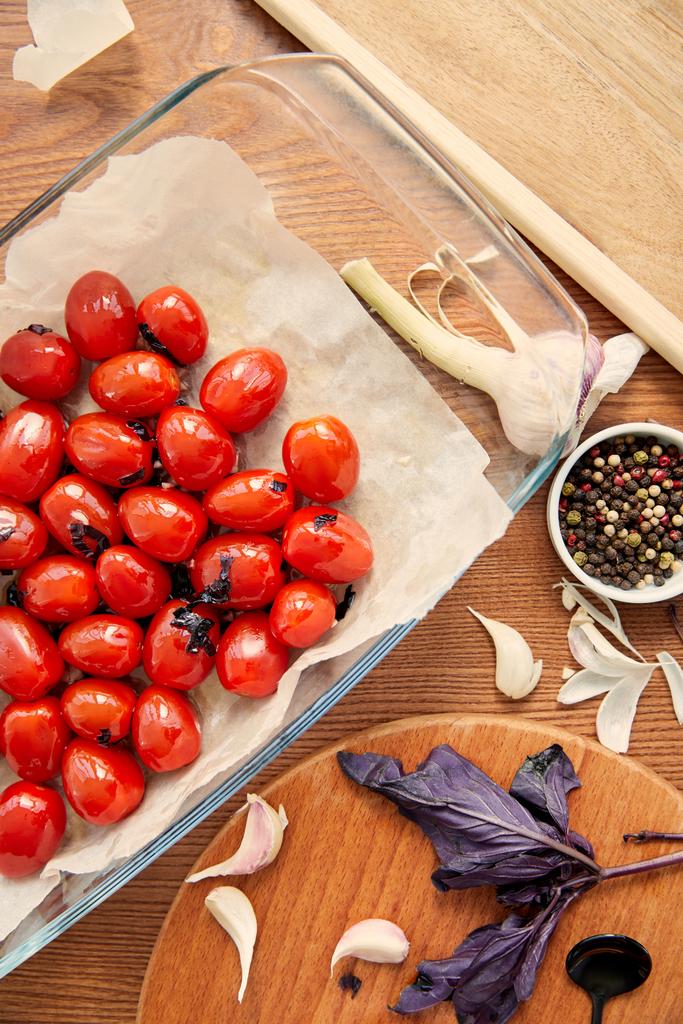 Vista superior de la bandeja para hornear con tomates cerca de tablas de cortar con ingredientes sobre fondo de madera
 - Foto, Imagen