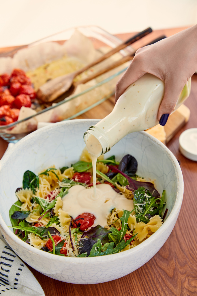 Vágott kilátás nő öntés majonéz tészta saláta tálban az asztalon izolált bézs - Fotó, kép