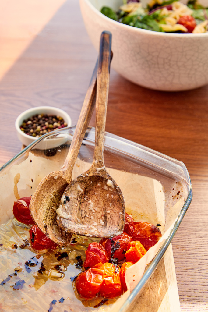 Nagy látószögű kilátás sütő tál spatulák és paradicsom vágódeszka közelében tálak paprika és tészta saláta fából készült háttér - Fotó, kép