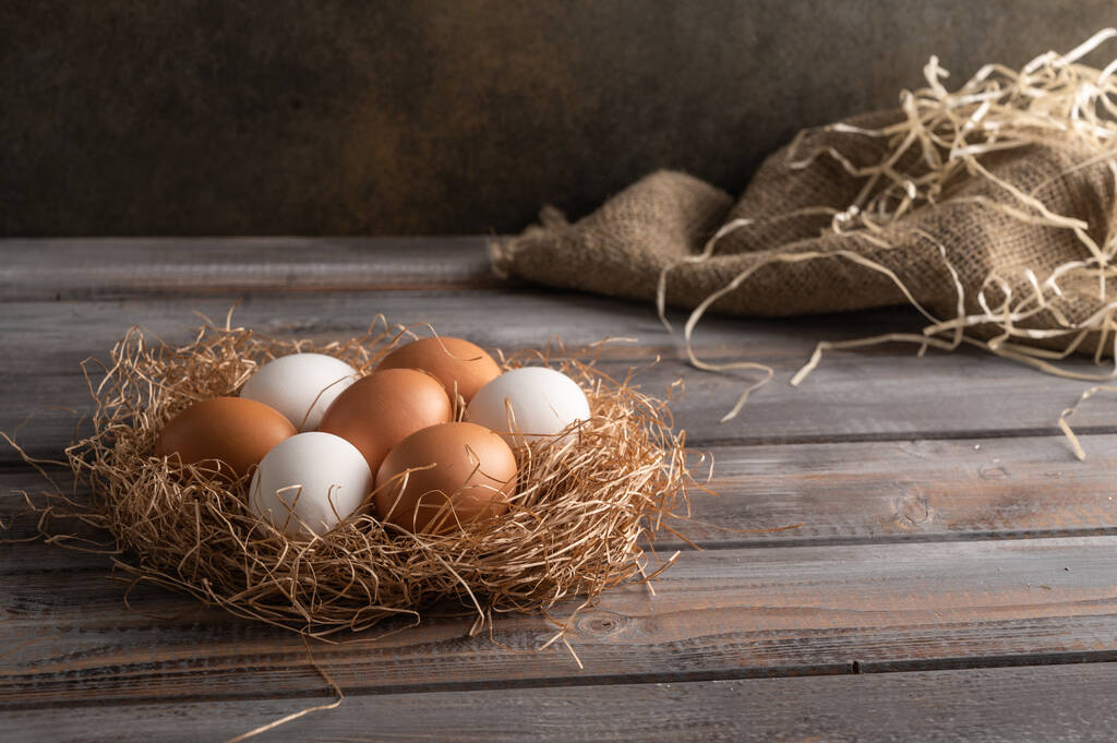 Huevos de pollo marrones y blancos en un nido de paja sobre fondo de madera. Estilo rústico
 - Foto, Imagen