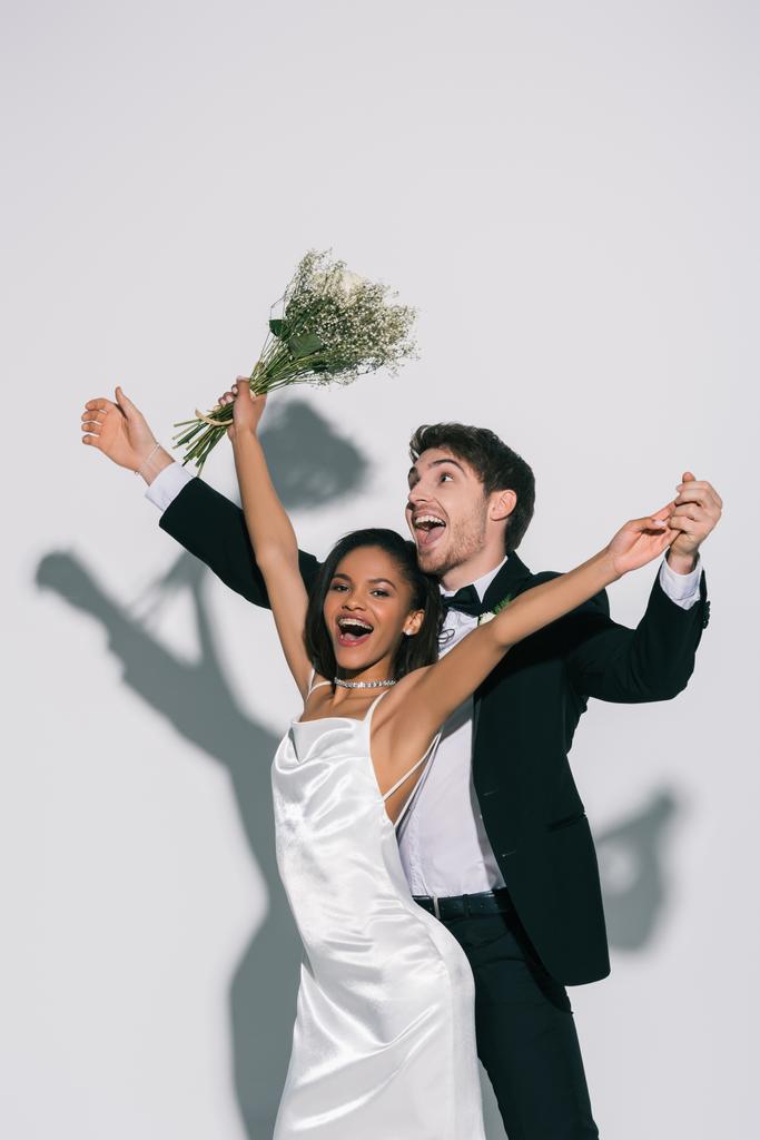 aufgeregte, elegante interrassische Brautpaare, die auf weißem Hintergrund tanzen - Foto, Bild