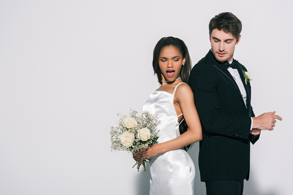 bonito noivo e atraente noiva afro-americana de pé de volta para trás no fundo branco
 - Foto, Imagem