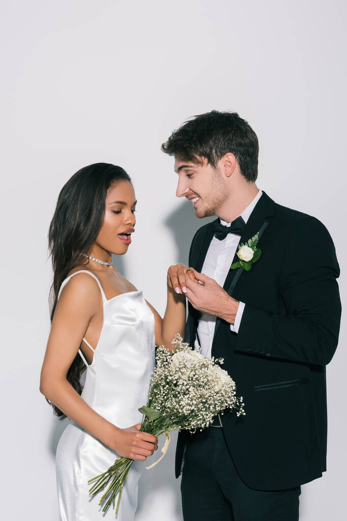 boldog vőlegény fogja a kezét izgatott afro-amerikai menyasszony fehér háttér - Fotó, kép