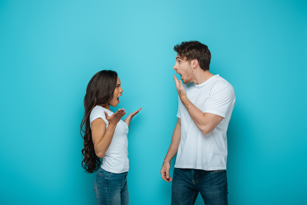 uomo scioccato che copre la bocca con mano vicino afro-americano ragazza litigando su sfondo blu
 - Foto, immagini