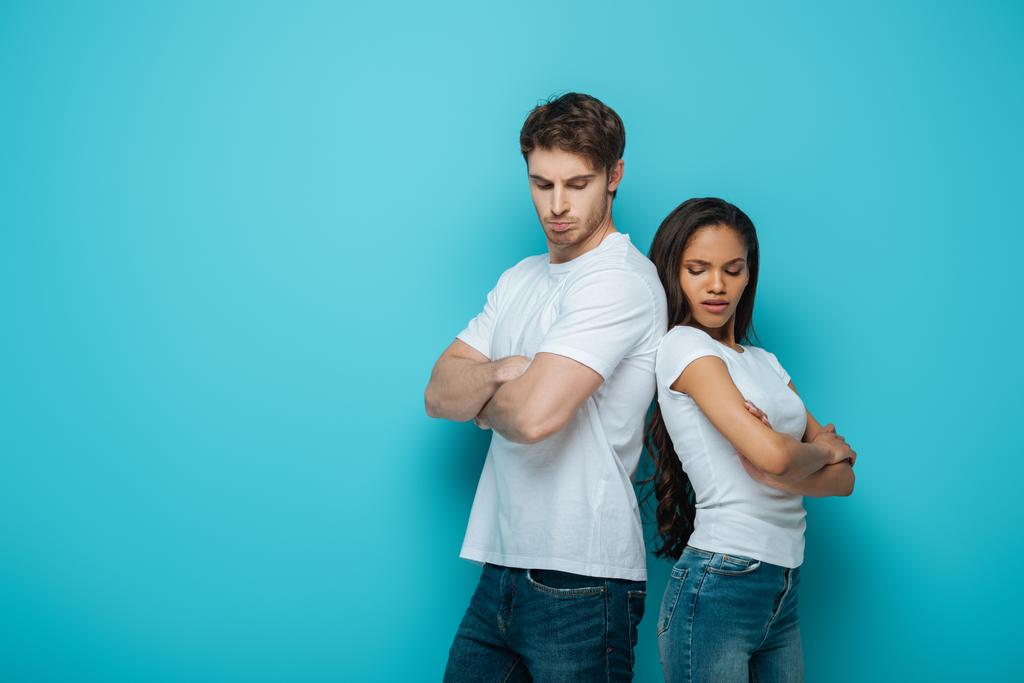 offended interracial couple standing back to back with crossed arms on blue background - Photo, Image