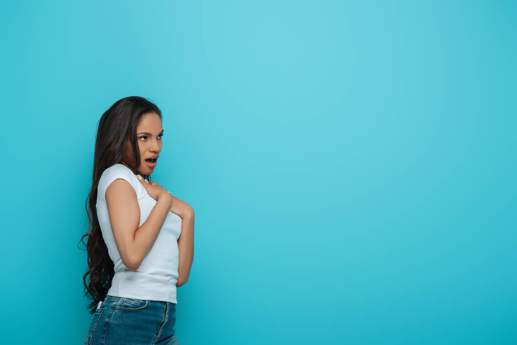 järkyttynyt afrikkalainen amerikkalainen tyttö koskettaa rintaa katsellen pois eristetty sininen
 - Valokuva, kuva