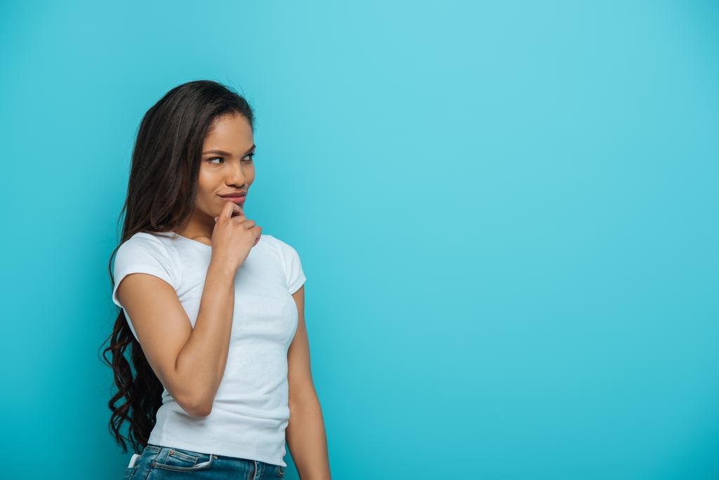 reflexiva afroamericana chica tocando la barbilla y mirando hacia otro lado aislado en azul
 - Foto, Imagen