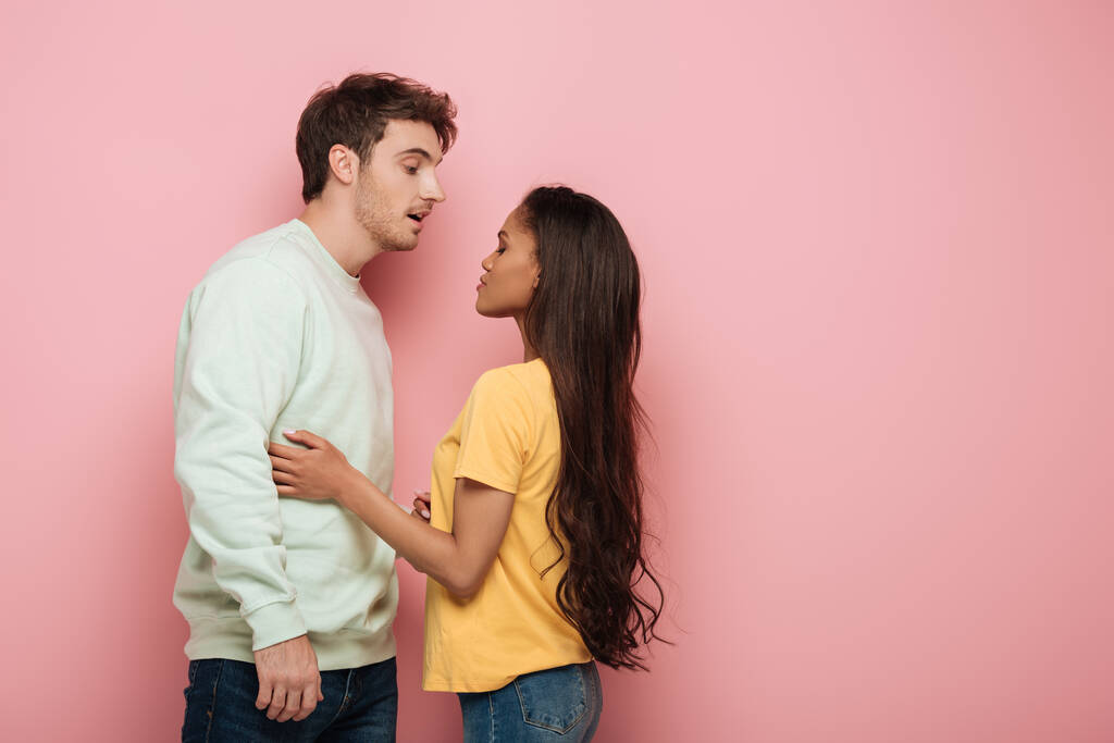 aantrekkelijk Afrikaans amerikaans meisje aanraken knappe vriend terwijl staande face to face op roze achtergrond - Foto, afbeelding