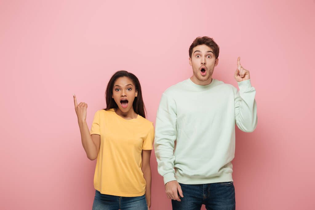excited interracial couple showing idea signs while looking at camera on pink background - Photo, Image