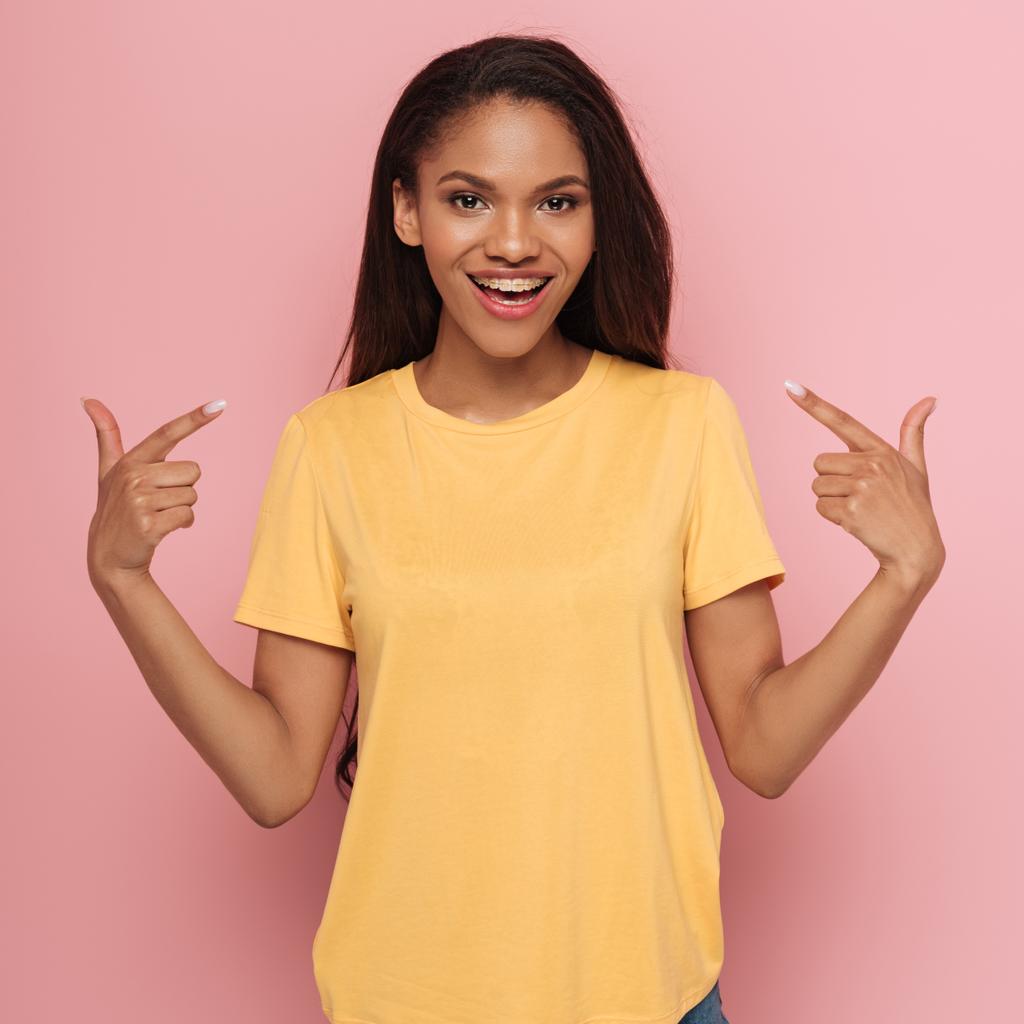 cheerful african american girl pointing with fingers at braces on her teeth on pink background - Photo, Image