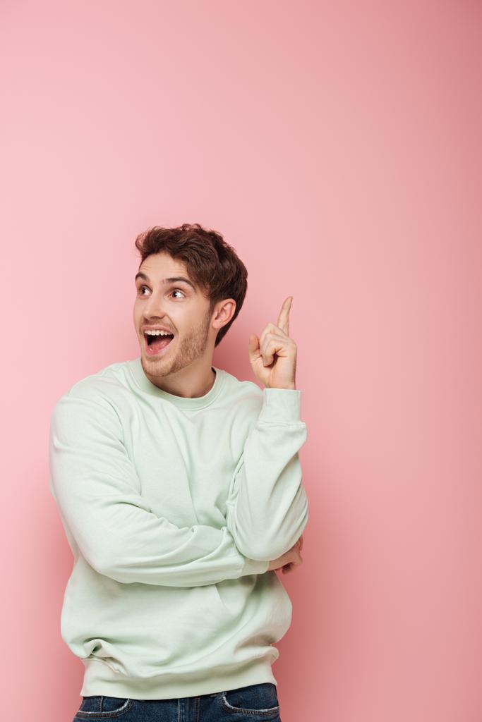 izgatott fiatalember áll nyitott szájjal, és bemutatja ötlet gesztus rózsaszín háttér - Fotó, kép