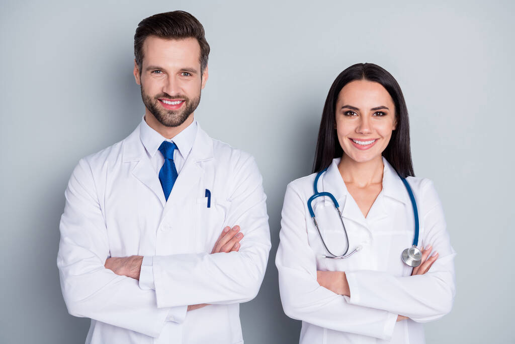 Фото красивого врача парень профессиональная женщина консультация пациента вирологическая клиника слушать клиента зубастые улыбающиеся руки скрещенные опытные врачи носят халаты изолированные серый цвет фона
 - Фото, изображение