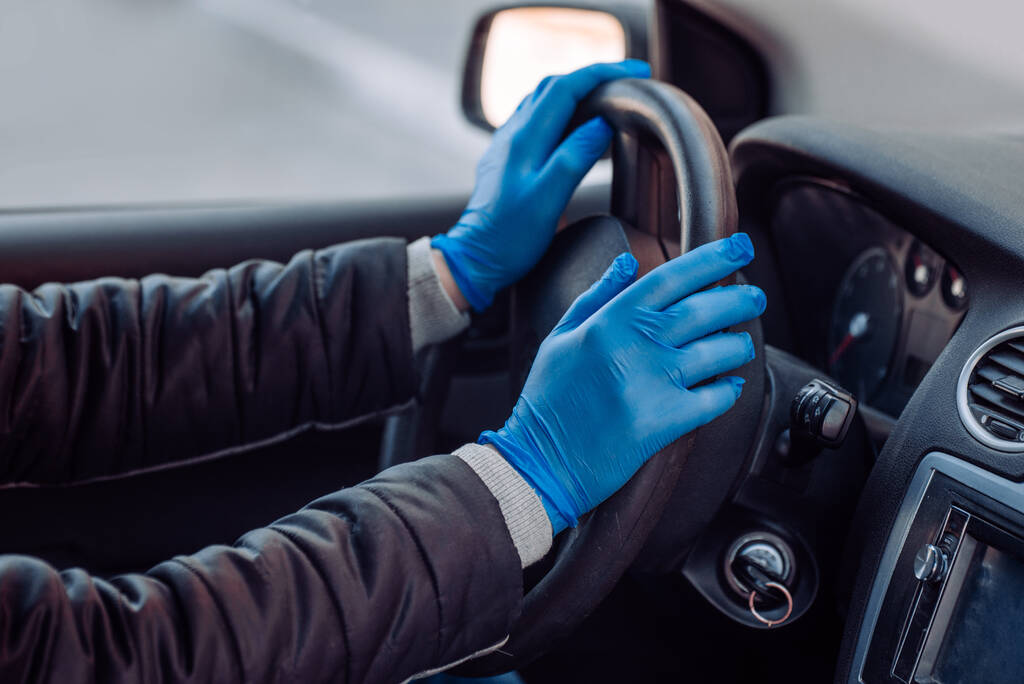 Un hombre sostiene el volante de un coche con guantes médicos protectores. Manos de cerca. Conducción segura en un taxi durante el coronavirus pandémico. Proteger al conductor y a los pasajeros de las bacterias y la infección por virus
 - Foto, imagen