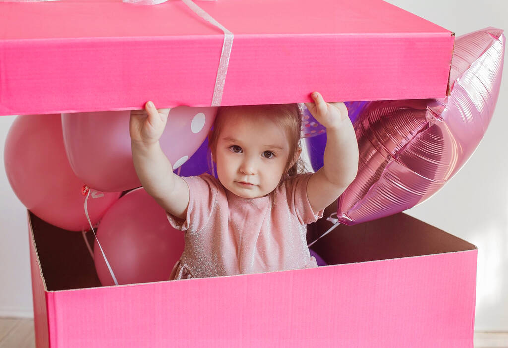 маленька красива дівчинка у великій рожевій подарунковій коробці з повітряними кулями
 - Фото, зображення