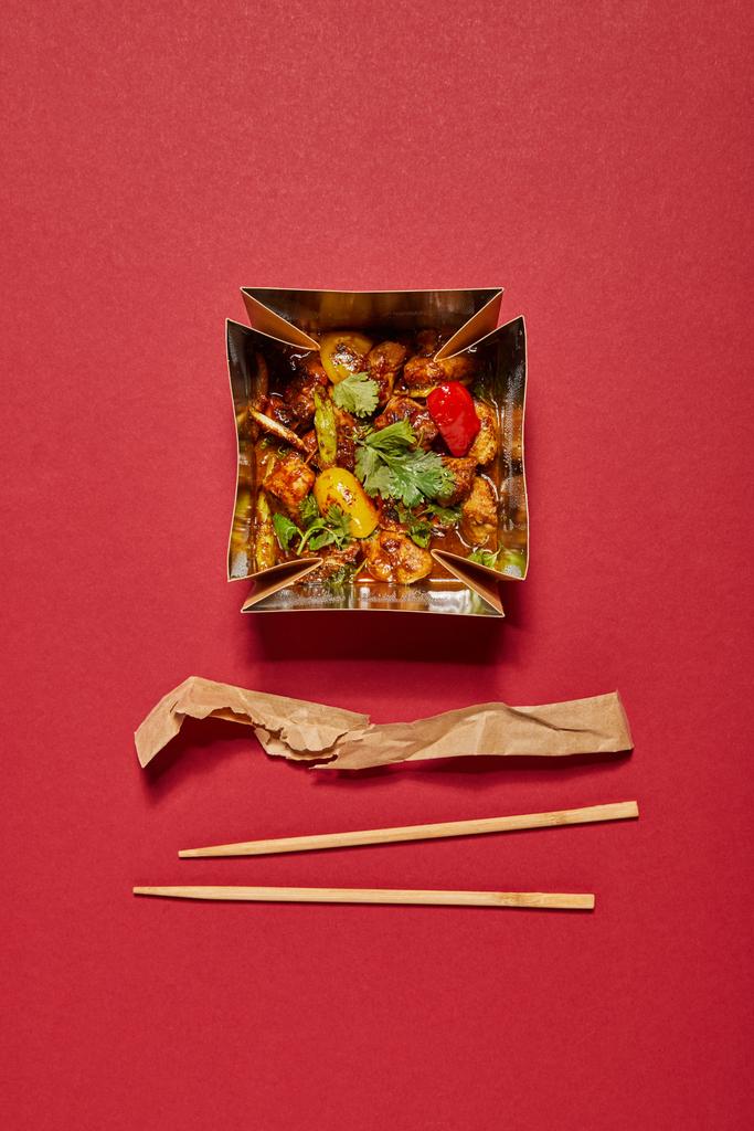 vista superior de palillos cerca de cerdo con salsa agridulce en caja para llevar en rojo
 - Foto, imagen