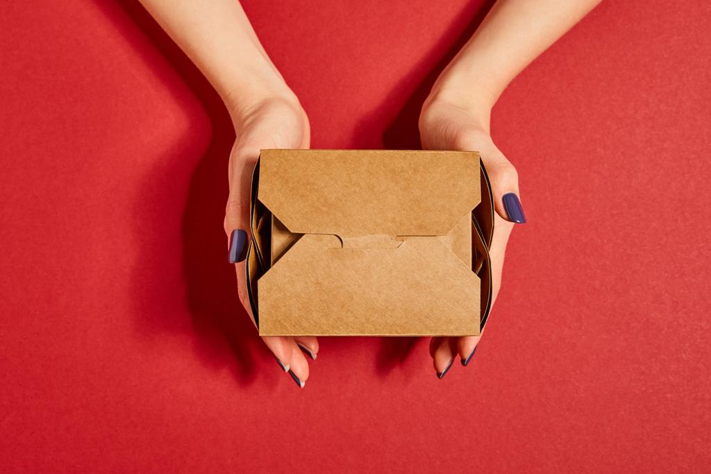 καλλιεργημένη άποψη της γυναίκας που κρατά κουτί πακέτο στο κόκκινο - Φωτογραφία, εικόνα